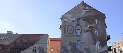 "1918", "100 år av självständigt" och Józef Pilsudski i profil. På en parkbänk mittemot denna vägg sitter...
